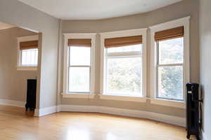 Empty room featuring plenty of natural light, radiator, and light hardwood / wood-style flooring