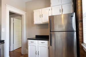 Kitchen with stainless steel fridge, white cabinetry, and dark hardwood / wood-style floors