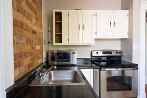 Kitchen featuring brick wall, sink, appliances with stainless steel finishes, and white cabinets