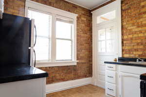 Kitchen with brick wall, sink, black fridge, and white cabinets