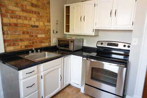 Kitchen featuring light tile patterned floors, sink, appliances with stainless steel finishes, brick wall, and white cabinets