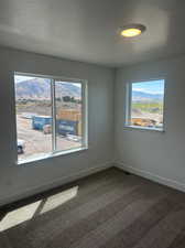 Carpeted empty room featuring a mountain view, a textured ceiling, and a healthy amount of sunlight