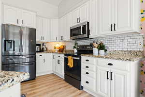 Kitchen featuring light wood-type flooring, light stone counters, stainless steel appliances, white cabinetry, and decorative backsplash