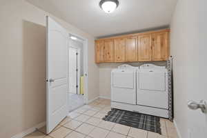 Clothes washing area featuring light tile patterned floors, cabinets, and washer and dryer