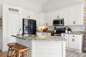 Kitchen with vaulted ceiling, light wood-type flooring, stainless steel appliances, white cabinetry, and a kitchen island with sink