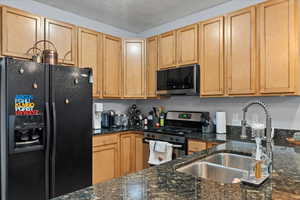 Kitchen with appliances with stainless steel finishes, a textured ceiling, sink, and dark stone counters