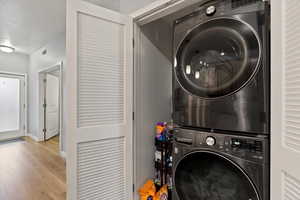 Clothes washing area featuring light wood-type flooring, stacked washing machine and dryer