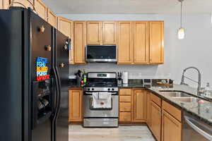 Kitchen featuring pendant lighting, stainless steel appliances, sink, light wood-type flooring, and dark stone counters