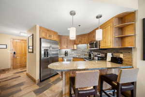 Kitchen featuring hanging light fixtures, hardwood / wood-style floors, appliances with stainless steel finishes, kitchen peninsula, and a breakfast bar