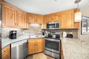 Kitchen featuring stainless steel appliances, light stone counters, sink, decorative backsplash, and light tile patterned flooring