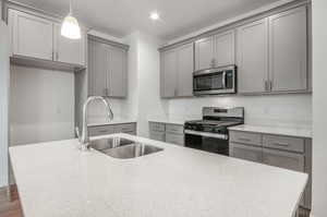 Kitchen with gray cabinets, hardwood / wood-style floors, sink, hanging light fixtures, and appliances with stainless steel finishes