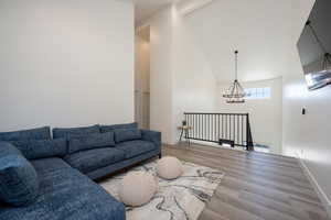 Living room featuring hardwood / wood-style flooring, an inviting chandelier, and vaulted ceiling