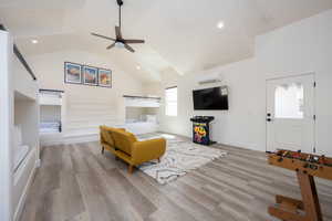 Living room with high vaulted ceiling, a wall mounted AC, ceiling fan, and light hardwood / wood-style floors