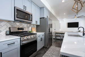 Kitchen with dark tile patterned flooring, backsplash, sink, ceiling fan, and appliances with stainless steel finishes