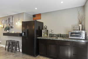 Kitchen featuring dark stone countertops, black fridge, dark brown cabinetry, and sink