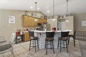 Kitchen featuring pendant lighting, lofted ceiling, a center island, appliances with stainless steel finishes, and a breakfast bar