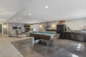 Playroom with pool table, a stone fireplace, sink, and concrete flooring