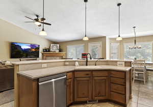 Kitchen featuring ceiling fan with notable chandelier, dishwasher, lofted ceiling, decorative light fixtures, and a kitchen island with sink