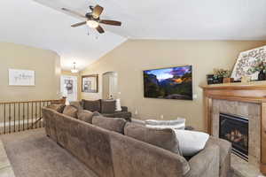 Living room with ceiling fan, a fireplace, and lofted ceiling