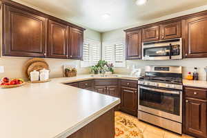 Kitchen with stainless steel appliances, sink, light tile patterned floors, and dark brown cabinets