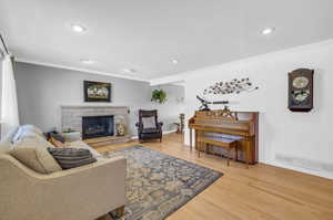 Living room with light hardwood wood flooring, molding, and a stone fireplace