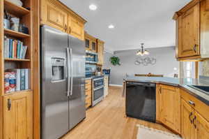 Kitchen featuring light wood-type flooring, appliances with stainless steel finishes, decorative backsplash, and a notable chandelier