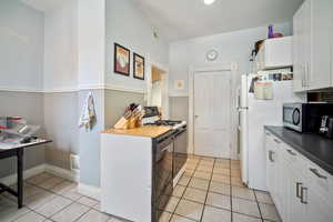 Kitchen with white cabinets, light tile patterned floors, white refrigerator, gas range, and black dishwasher