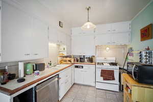 Kitchen featuring white range with gas stovetop, light tile patterned floors, white cabinetry, and stainless steel dishwasher