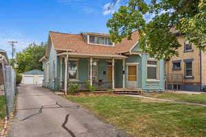 View of front of home featuring a porch, a garage, a front lawn, and an outbuilding