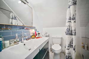 Bathroom with vanity, a shower with shower curtain, vaulted ceiling, toilet, and tile patterned floors