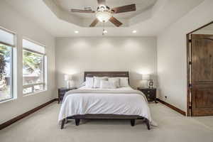 Carpeted bedroom featuring ceiling fan and a tray ceiling