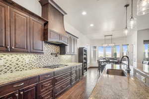 Kitchen featuring light stone countertops, stainless steel gas stovetop, hanging light fixtures, dark wood-type flooring, and sink