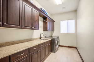 Clothes washing area featuring washer and dryer, cabinets, and sink