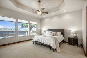 Bedroom with light colored carpet, ceiling fan, and a tray ceiling