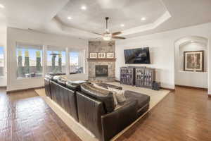 Living room with a tray ceiling, hardwood / wood-style floors, ceiling fan, and a stone fireplace