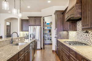 Kitchen with decorative light fixtures, stainless steel appliances, sink, premium range hood, and dark hardwood / wood-style floors