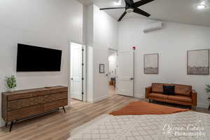 Living room featuring light wood-type flooring, a wall mounted AC, ceiling fan, and high vaulted ceiling