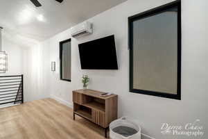 Living room featuring a wall mounted air conditioner, a textured ceiling, ceiling fan, lofted ceiling, and light hardwood / wood-style floors