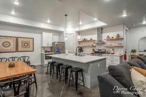 Kitchen featuring an island with sink, sink, a breakfast bar, wall chimney exhaust hood, and appliances with stainless steel finishes