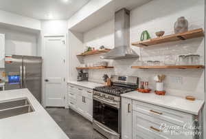 Kitchen featuring backsplash, stainless steel appliances, wall chimney exhaust hood, and white cabinetry