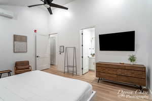 Bedroom with connected bathroom, light wood-type flooring, ceiling fan, and a wall mounted air conditioner