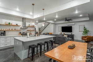 Kitchen featuring tasteful backsplash, ceiling fan, a breakfast bar area, a center island with sink, and wall chimney range hood