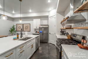 Kitchen with stainless steel appliances, white cabinetry, sink, island exhaust hood, and pendant lighting