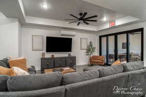 Living room with a wall mounted AC, a textured ceiling, ceiling fan, a raised ceiling, and hardwood / wood-style flooring