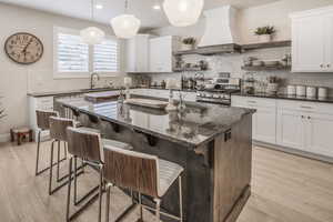 Kitchen with dark stone countertops, appliances with stainless steel finishes, a center island with sink, and custom exhaust hood