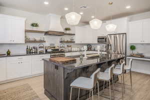 Kitchen featuring dark stone countertops, custom range hood, an island with sink, and stainless steel appliances