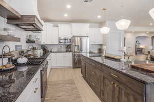 Kitchen featuring dark brown cabinets, light hardwood / wood-style flooring, stainless steel appliances, white cabinetry, and dark stone countertops