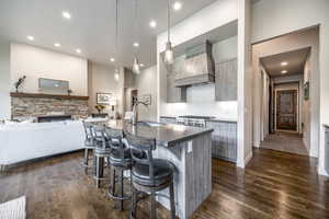 Kitchen featuring dark hardwood / wood-style flooring, custom range hood, sink, a center island with sink, and a breakfast bar area