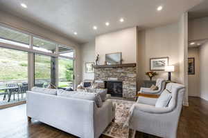 Living room with a textured ceiling, a stone fireplace, and dark wood-type flooring