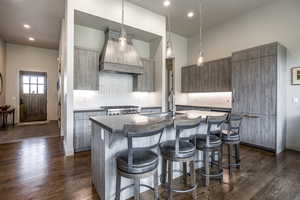 Kitchen featuring a kitchen island with sink, dark wood-type flooring, and custom range hood